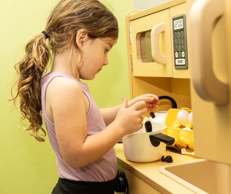 Young girl practicing pivotal life skills by playing with a toy kitchen during ABA therapy at home