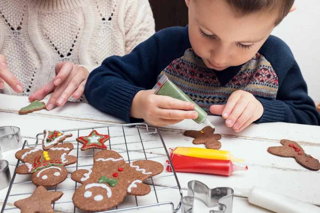 A child decorating gingerbread cookies with icing alongside an adult, featuring festive designs on the cookies like stars and Christmas trees, capturing a fun, hands-on activity perfect for family bonding, associated with ABS Kids.