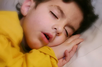 A young child peacefully sleeping, wearing a yellow shirt, representing restful sleep, a topic often addressed in programs for children with autism, associated with ABS Kids.