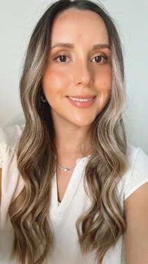 Milena Suarez, smiling and wearing a white top, with long, wavy brown hair and a necklace, in front of a neutral background.